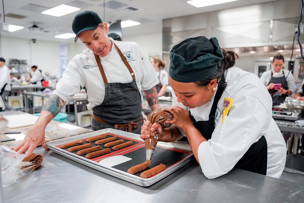 Culinary arts student piping eclairs with instructor
