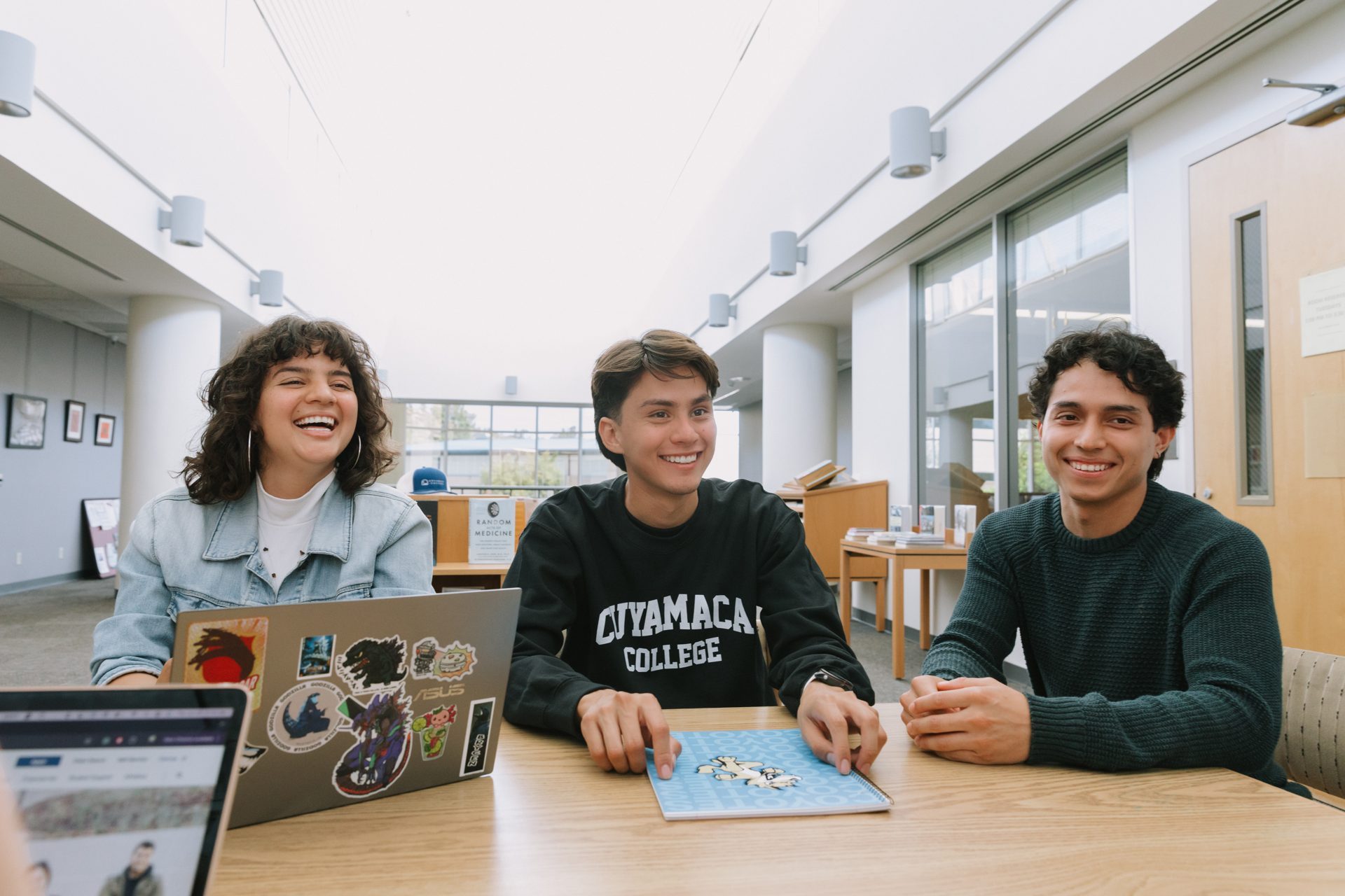Three students studying together at a table and smiling, one wearing a Cuyamaca College sweatshirt