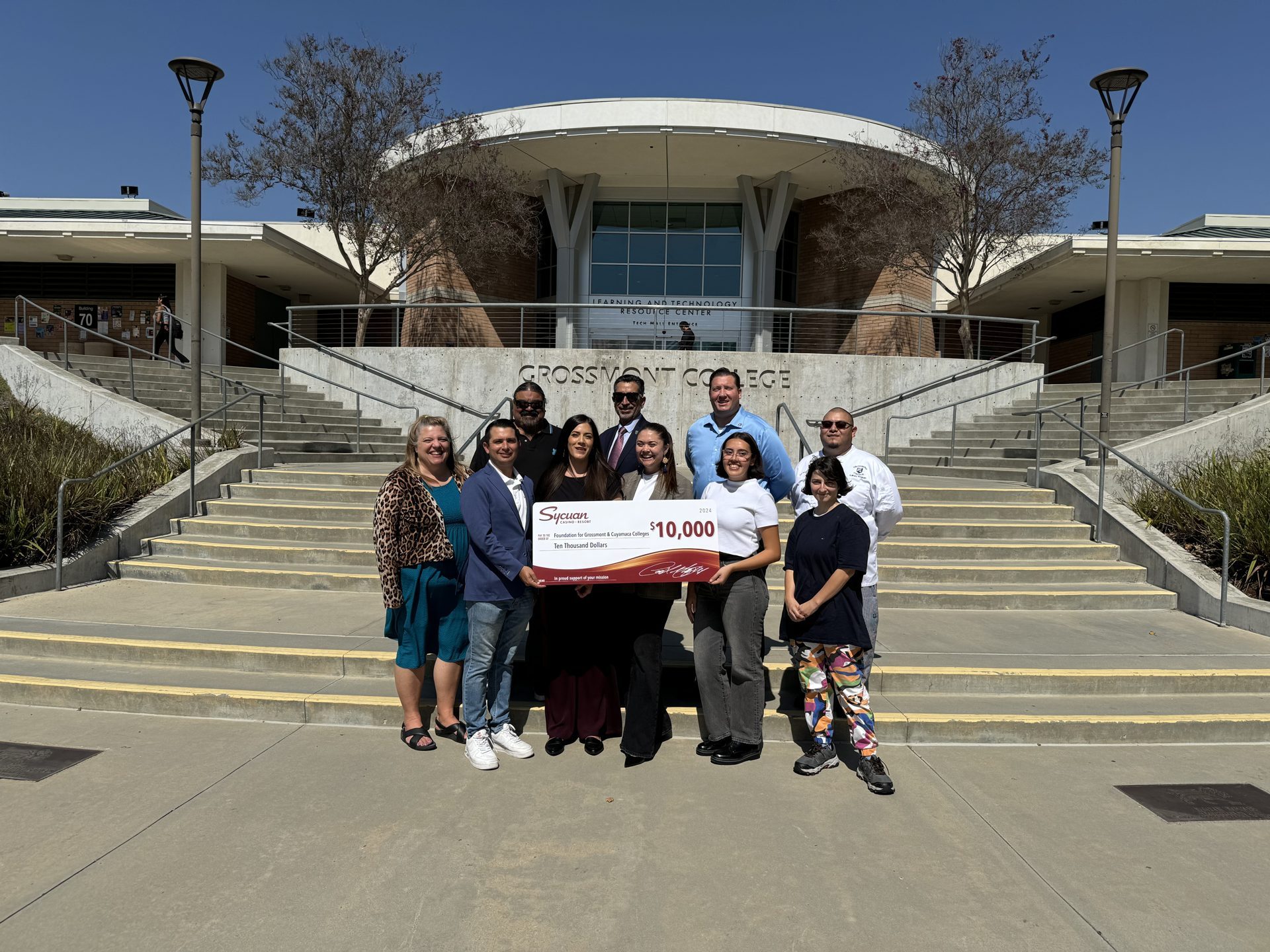 A group of about nine people on the Grossmont College steps holding a large ceremonial $10,000 check